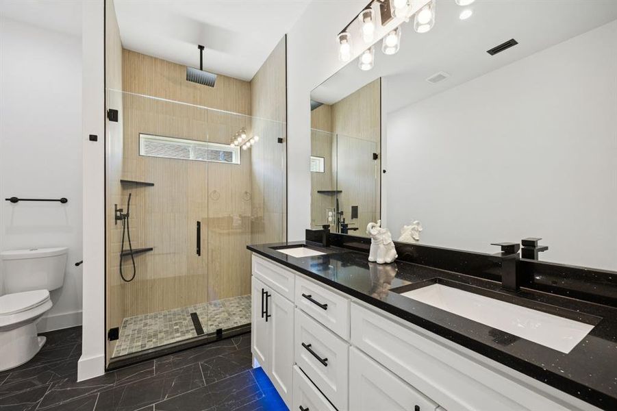 Full bathroom featuring a shower stall, double vanity, and dark marble finish flooring