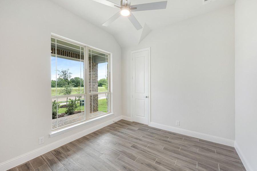 Empty bedroom with vaulted ceiling, ceiling fan, wood-look floors, and large window with yard view