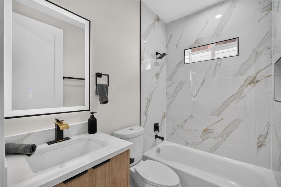 Sleek bathroom featuring elegant marble-patterned tiles, a modern vanity with gold fixtures, and a backlit mirror, creating a luxurious and contemporary feel.