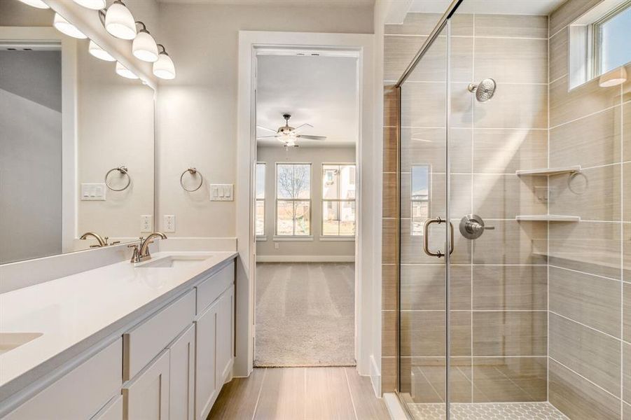 Full bath with double vanity, a shower stall, a ceiling fan, and light carpet