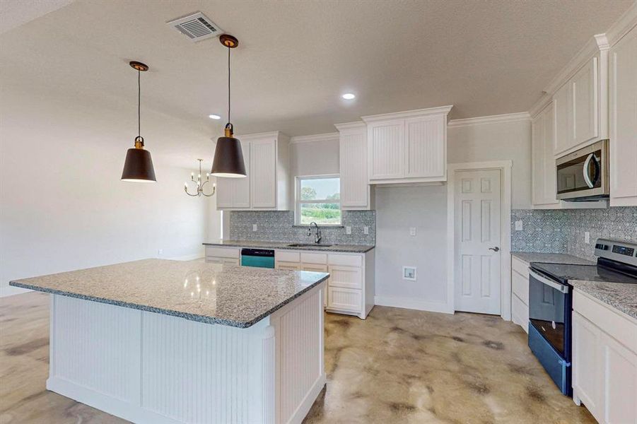 Kitchen with light stone counters, decorative light fixtures, a kitchen island, stainless steel appliances, and white cabinets