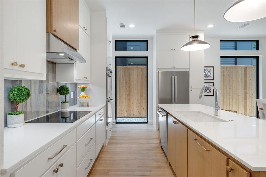 Kitchen with white cabinets, sink, decorative light fixtures, ventilation hood, and appliances with stainless steel finishes