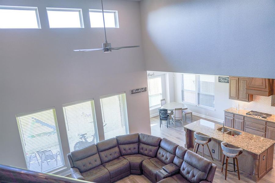 Living room with a ceiling fan, light wood finished floors, and a towering ceiling