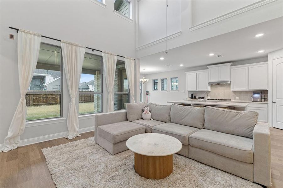 Living area featuring light wood-style floors, a chandelier, and a high ceiling Living area featuring light wood-style floors, a chandelier, and a high ceiling