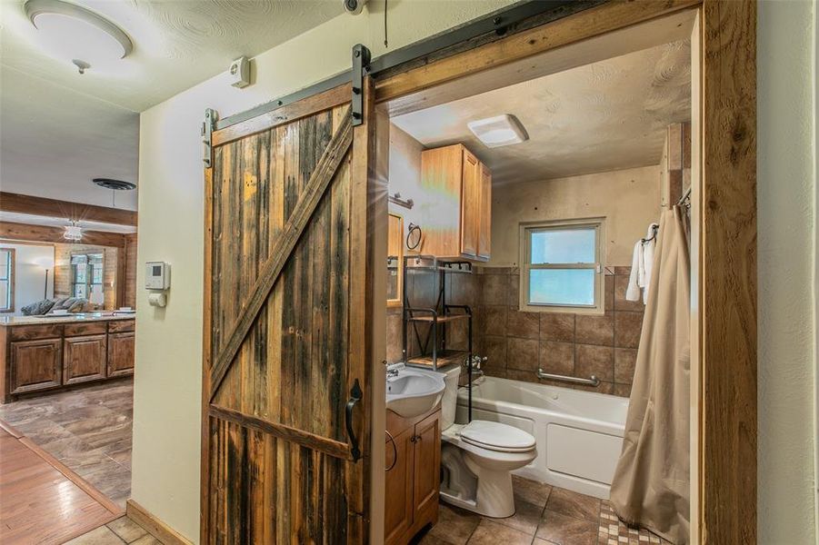 Full guest bathroom featuring rustic barn door accents and a tub/shower combination. Full guest bathroom featuring rustic barn door accents and a tub/shower combination.