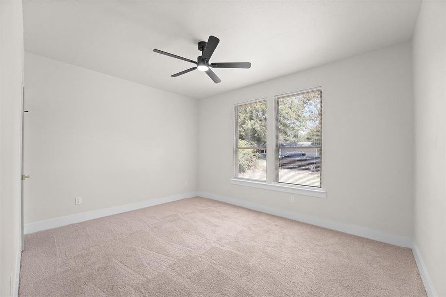 Bright room featuring two large windows, neutral-toned carpet, a ceiling fan with integrated lighting, and white baseboards Bright room featuring two large windows, neutral-toned carpet, a ceiling fan with integrated lighting, and white baseboards