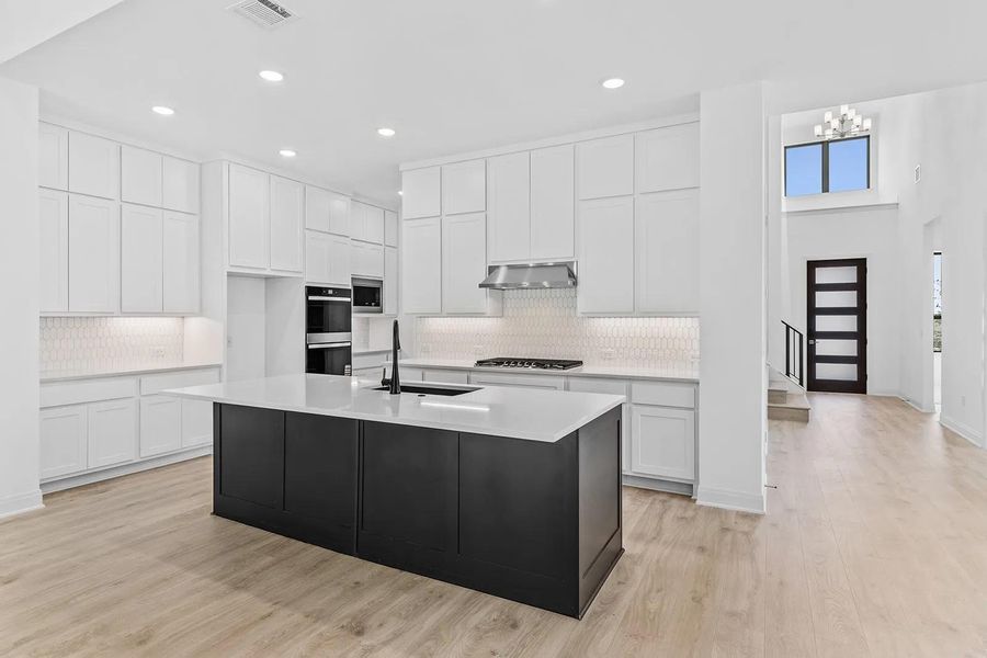 Kitchen with white cabinetry, light wood finished floors, a center island with sink, backsplash, and recessed lighting