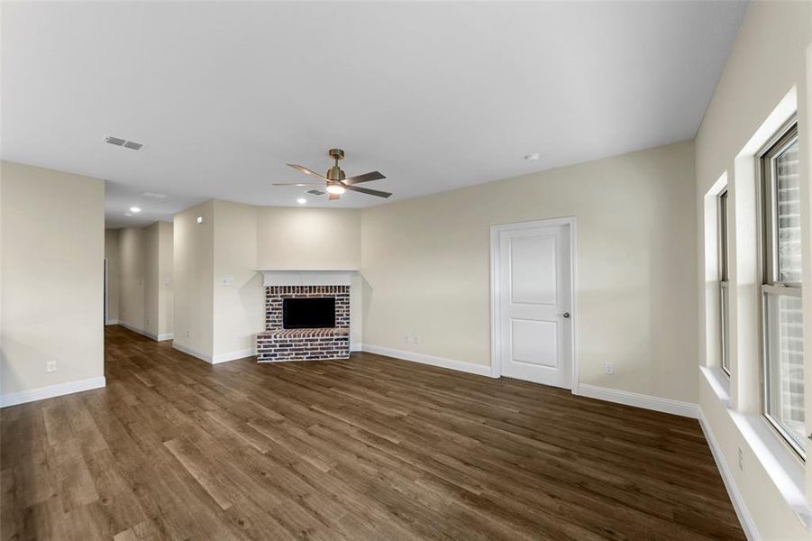 Spacious interior room featuring wood-finish flooring, a brick fireplace with a white mantle, an overhead ceiling fan, recessed lighting, and multiple windows