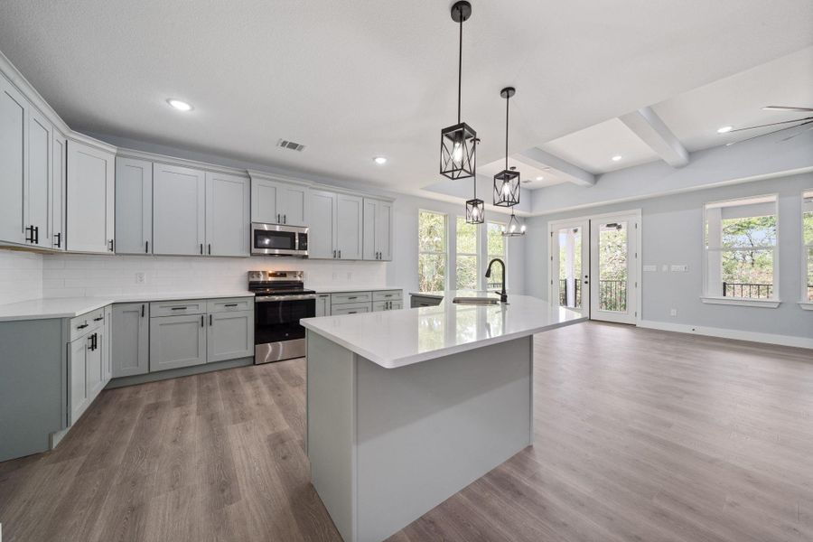 Open-concept kitchen and living area featuring wood-finish flooring, recessed lighting, and a tray ceiling with exposed beams