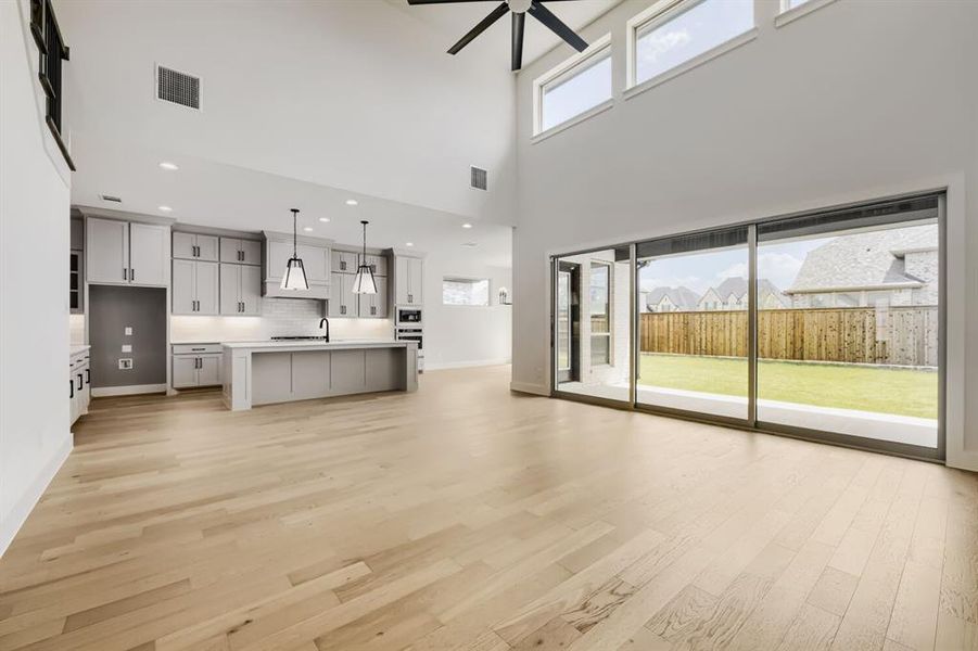 Open-concept living space featuring wood-finish flooring, a contemporary kitchen with a center island, high ceilings, transom windows, and a sliding glass door opening to a private backyard with a wood fence Open-concept living space featuring wood-finish flooring, a contemporary kitchen with a center island, high ceilings, transom windows, and a sliding glass door opening to a private backyard with a wood fence