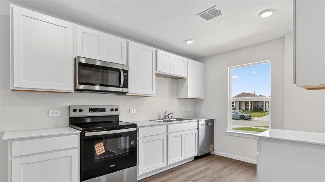 Kitchen featuring white shaker cabinetry, stainless steel appliances, light countertops, wood-finish flooring, and recessed lighting