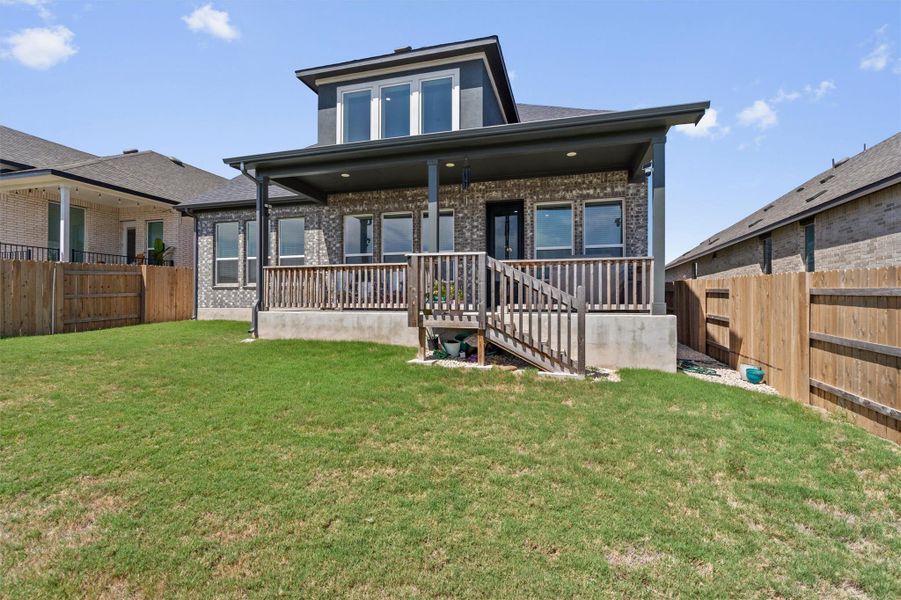 A wooden deck steps down to a green lawn enclosed by privacy fencing.