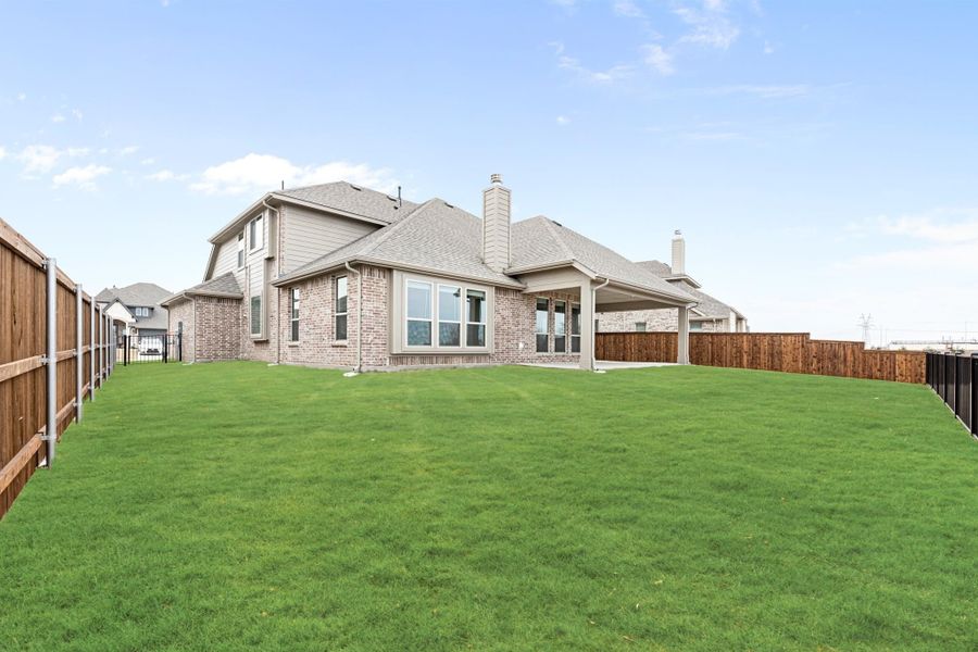 Back of two-story brick home with large fenced yard, covered patio, and chimney Back of two-story brick home with large fenced yard, covered patio, and chimney