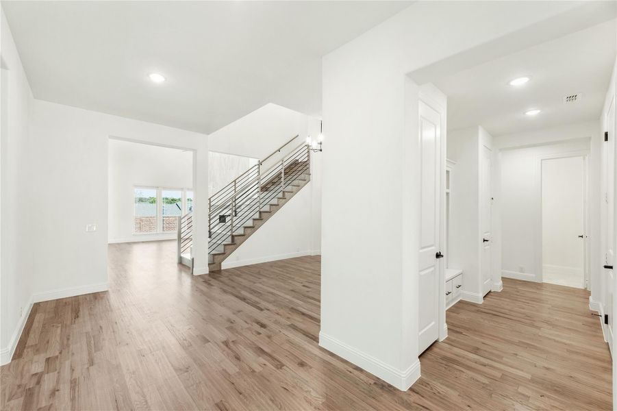 Open entryway and living area with hardwood floors, white walls, and modern staircase with metal railing