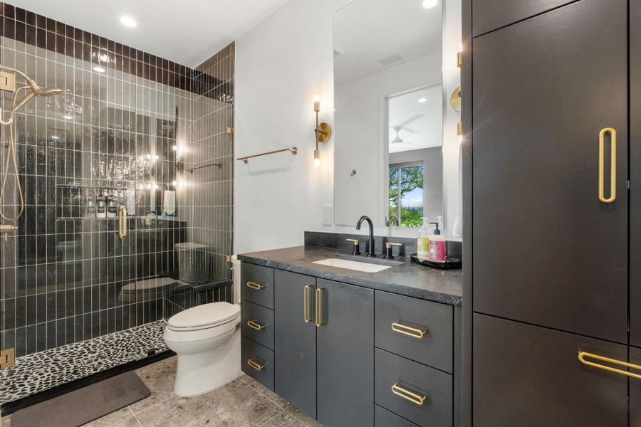 Modern bathroom featuring a glass-enclosed shower with vertical dark tile and a pebbled floor