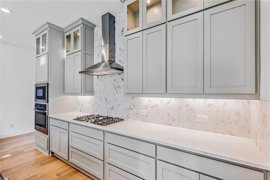 Kitchen with built in microwave, gray cabinetry, stainless steel oven, gas stovetop, and wall chimney exhaust hood