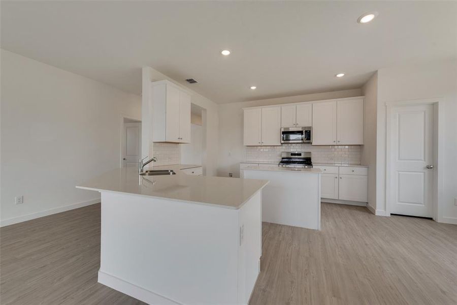 Kitchen with light wood-type flooring, decorative backsplash, a kitchen island with sink, stainless steel appliances, and white cabinets