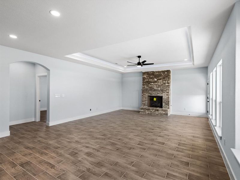 Unfurnished living room featuring ceiling fan, a raised ceiling, recessed lighting, wood finished floors, and arched walkways