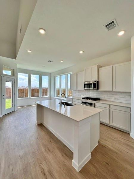 Kitchen featuring a large central island with a sink and a quartz countertop, white shaker cabinetry, stainless steel appliances, and a subway tile backsplash Kitchen featuring a large central island with a sink and a quartz countertop, white shaker cabinetry, stainless steel appliances, and a subway tile backsplash