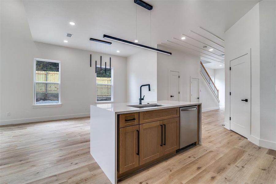 Kitchen featuring hanging light fixtures, brown cabinets, recessed lighting, light wood finished floors, and a center island with sink