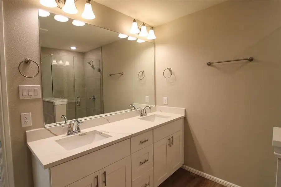 Bathroom featuring double vanity, a stall shower, dark wood finished floors, and a textured wall