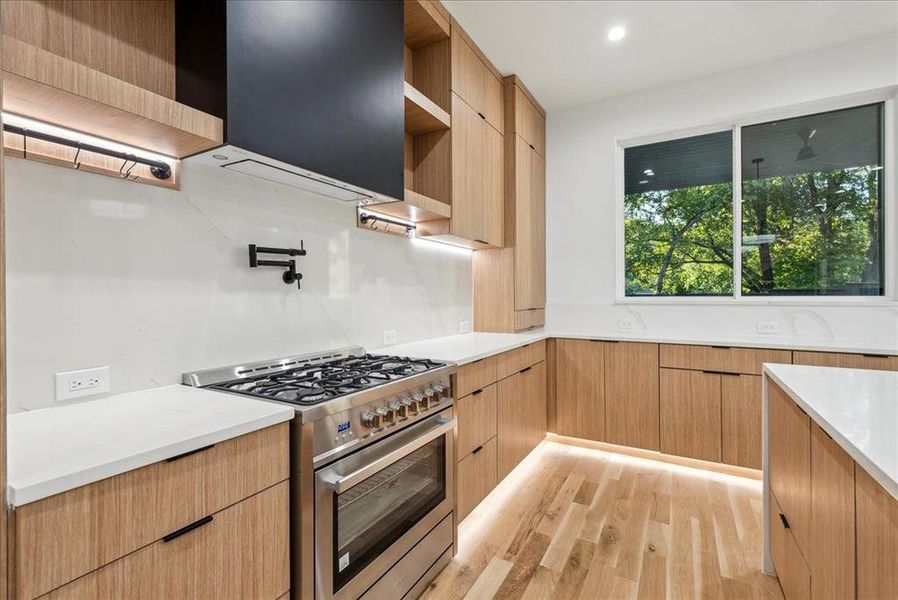 Kitchen featuring light brown cabinetry, light hardwood / wood-style flooring, and high end stainless steel range oven