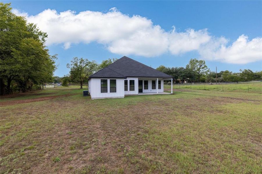 Back of property with cooling unit, a rural view, and a yard