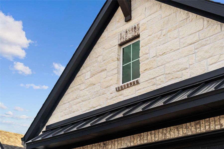 This striking gabled exterior showcases a sophisticated blend of textured cream-colored stone and rustic brick, all sharply framed by modern dark trim.