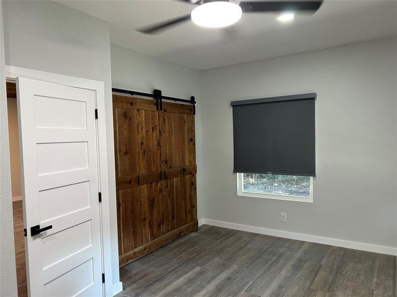 Unfurnished bedroom featuring dark wood-style floors, ceiling fan, and a barn door Unfurnished bedroom featuring dark wood-style floors, ceiling fan, and a barn door