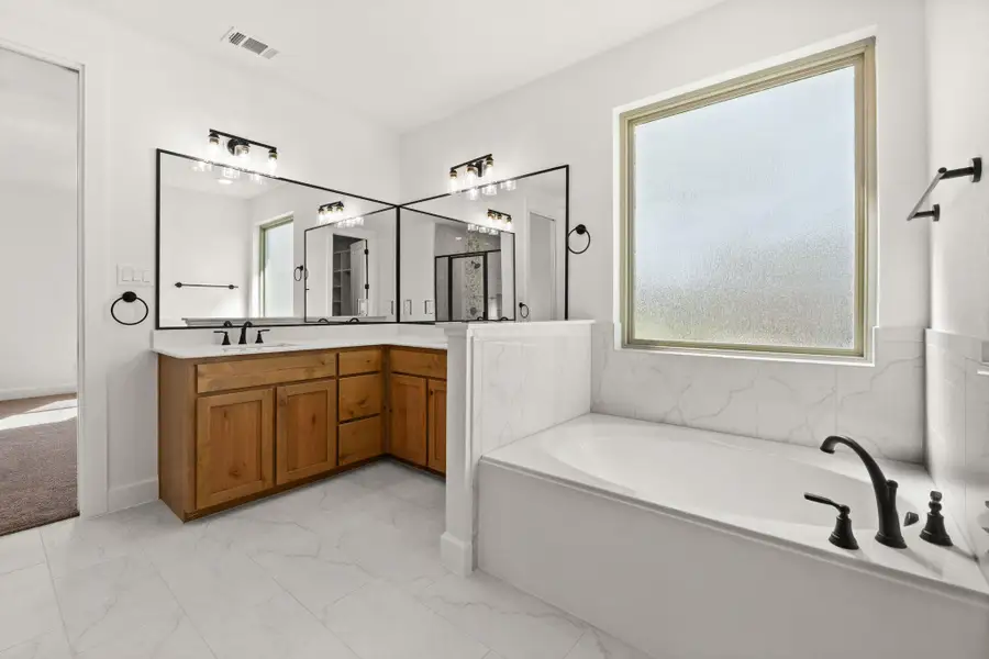 Full bath featuring a garden tub, double vanity, and light marble finish floors