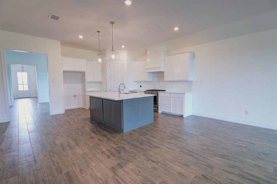 Kitchen featuring gas stove, a sink, custom exhaust hood, white cabinets, and a kitchen island with sink