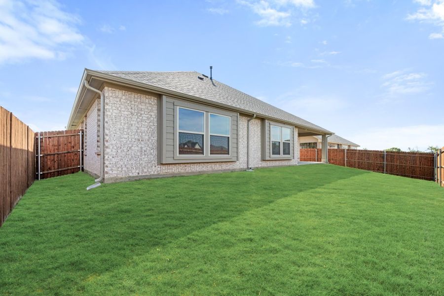 Rear exterior of single-story brick home with large fenced backyard and green lawn