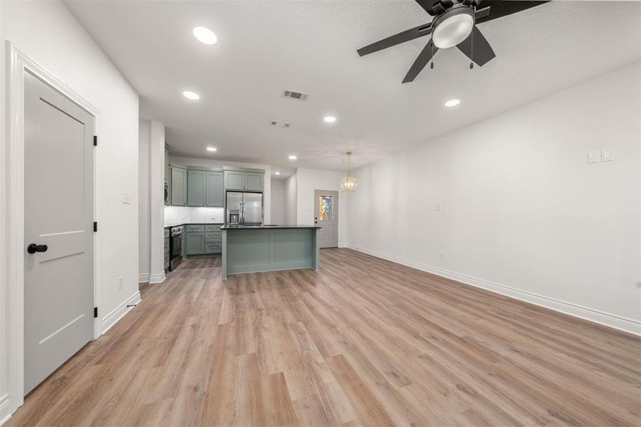 Kitchen with green cabinetry, dark countertops, open floor plan, recessed lighting, and light wood-style floors Kitchen with green cabinetry, dark countertops, open floor plan, recessed lighting, and light wood-style floors