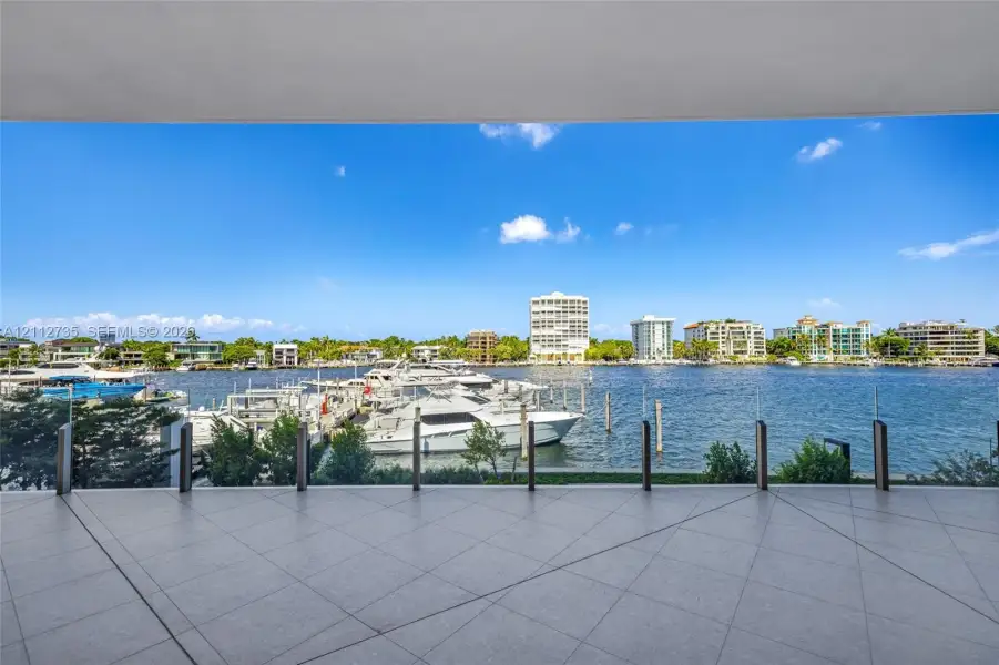 Covered terrace featuring large-format porcelain tile flooring and a transparent glass railing overlooking the waterfront