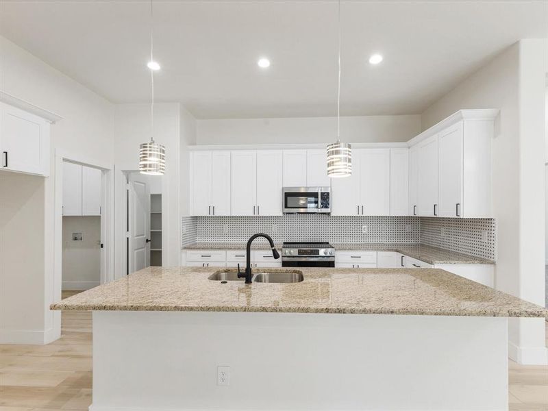 Kitchen with light wood finished floors, decorative light fixtures, backsplash, and stainless steel appliances