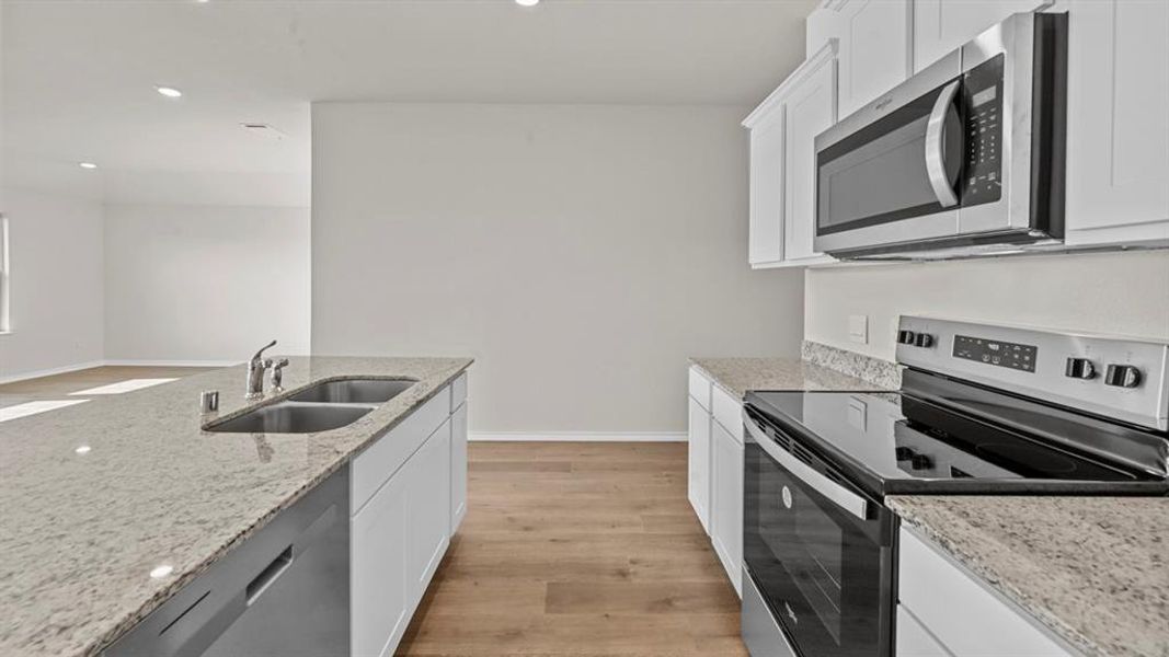 Kitchen with stainless steel appliances, white cabinets, light wood-type flooring, light stone counters, and recessed lighting