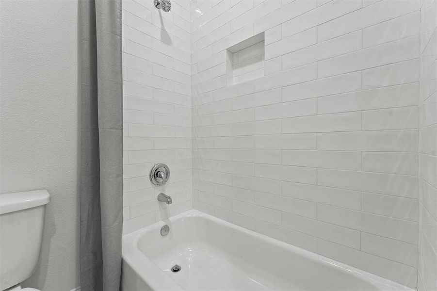 The bathroom features a clean, white subway-tiled shower area with a built-in niche for toiletries, a white bathtub, and a single shower head.