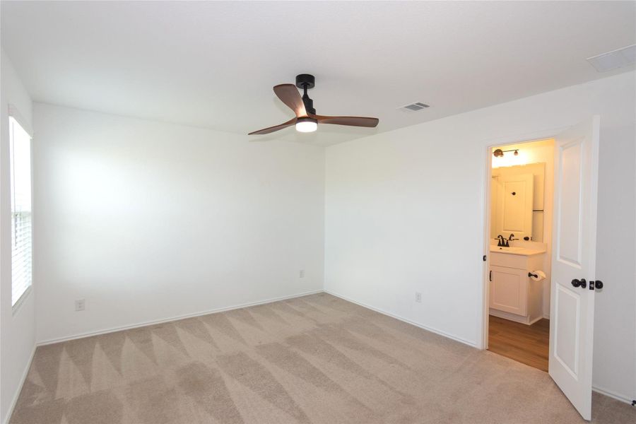 Spacious primary bedroom featuring neutral carpeting, a ceiling fan with integrated lighting, and a window with horizontal blinds