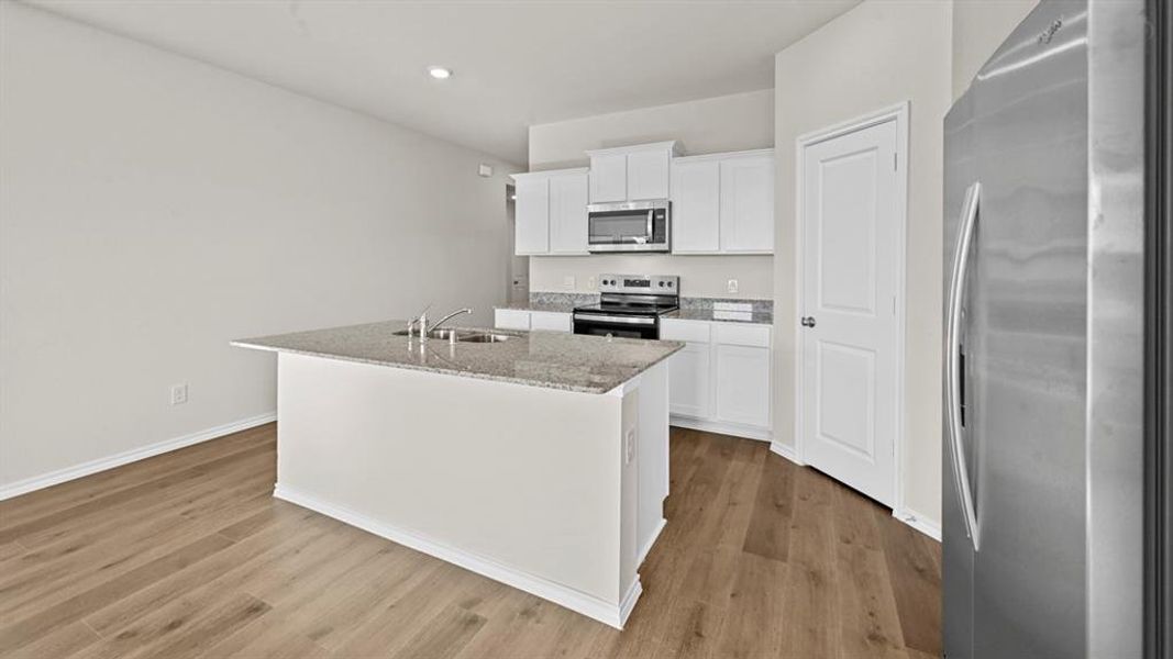 Kitchen featuring stainless steel appliances, white cabinets, a center island with sink, light stone countertops, and light wood-type flooring