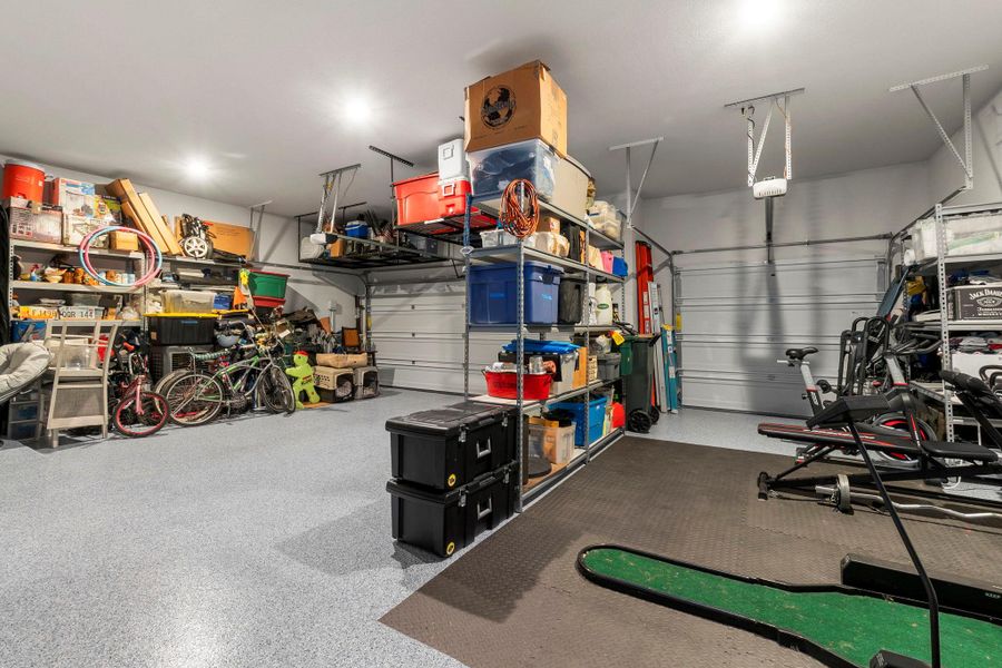 Spacious garage featuring a durable epoxy-coated concrete floor, recessed ceiling lighting, two overhead garage doors, and built-in shelving systems