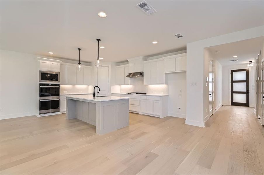 Kitchen with appliances with stainless steel finishes, white cabinetry, an island with sink, and light wood-type flooring