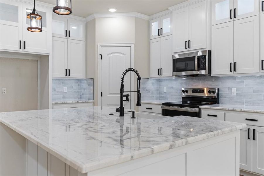 Kitchen with white cabinetry, hanging light fixtures, backsplash, an island with sink, and appliances with stainless steel finishes