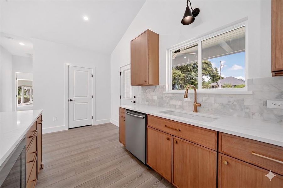 Kitchen featuring light wood-finish cabinetry, light stone countertops, a tile backsplash, and a stainless steel dishwasher