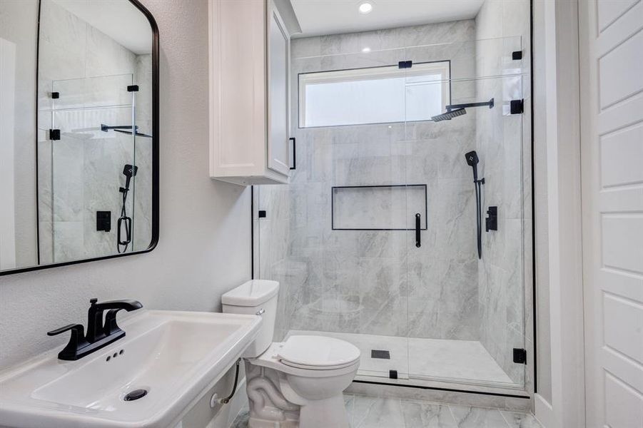 Walk-in shower with clear glass enclosure and black hardware, featuring a rainfall showerhead and separate handheld sprayer