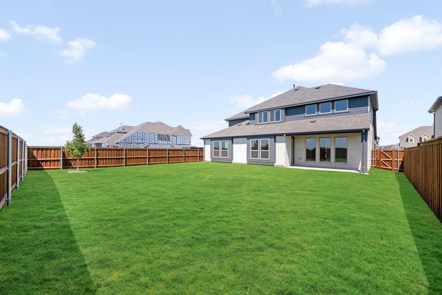 Backyard of two-story home with large green lawn, wood privacy fence, and covered patio with large windows.