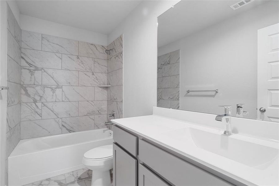 Secondary bathroom features light countertops and grey cabinets, neutral paint, shower/tub combo with tile surround, large mirror, tile floors, sleek fixtures and modern finishes, plenty of space to accommodate any visiting family or guests.