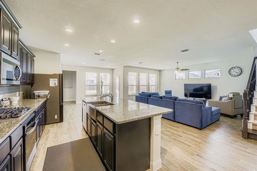 Kitchen with light wood-style flooring, open floor plan, light stone countertops, appliances with stainless steel finishes, and a textured ceiling Kitchen with light wood-style flooring, open floor plan, light stone countertops, appliances with stainless steel finishes, and a textured ceiling