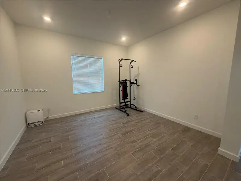 Neutral-toned interior space featuring wood-finish flooring, recessed lighting, and a single window with horizontal blinds
