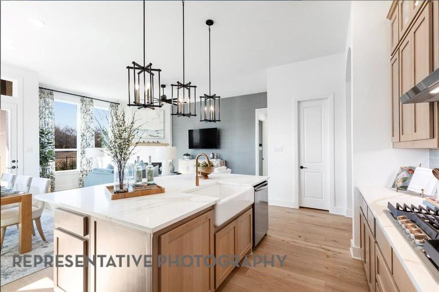 Kitchen featuring light brown cabinetry, open floor plan, light wood-style flooring, pendant lighting, and stainless steel appliances
