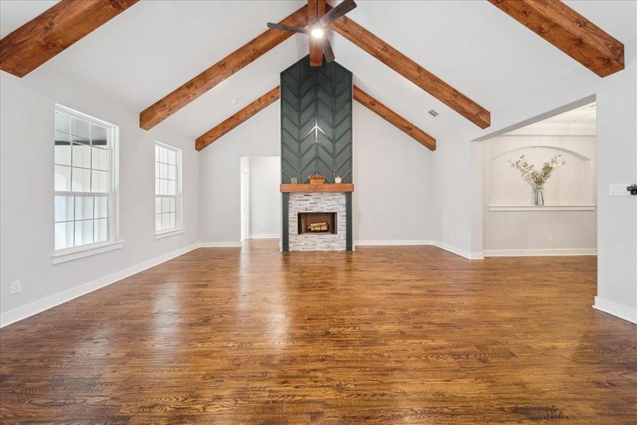 Unfurnished living room featuring dark hardwood / wood-style flooring, a stone fireplace, and beamed ceiling